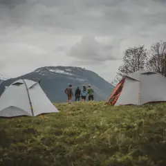 Dwa namioty na trawiastym zboczu górskim, z ludźmi stojącymi w tle.